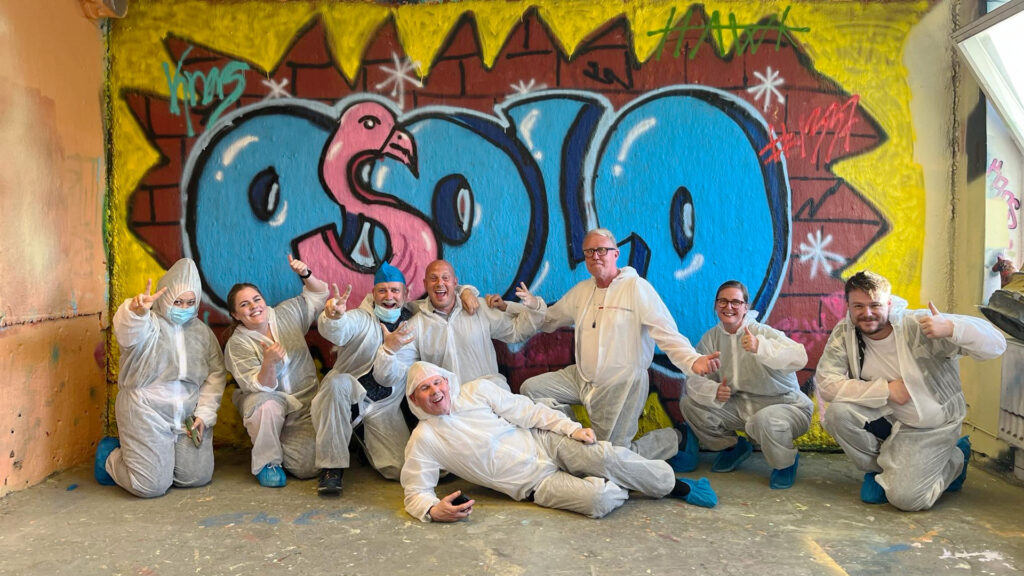 Anställda på strategiska webbyrån Osolo har målat graffiti på en vägg. Alla poserar framför målningen med en logotyp och flamingo.