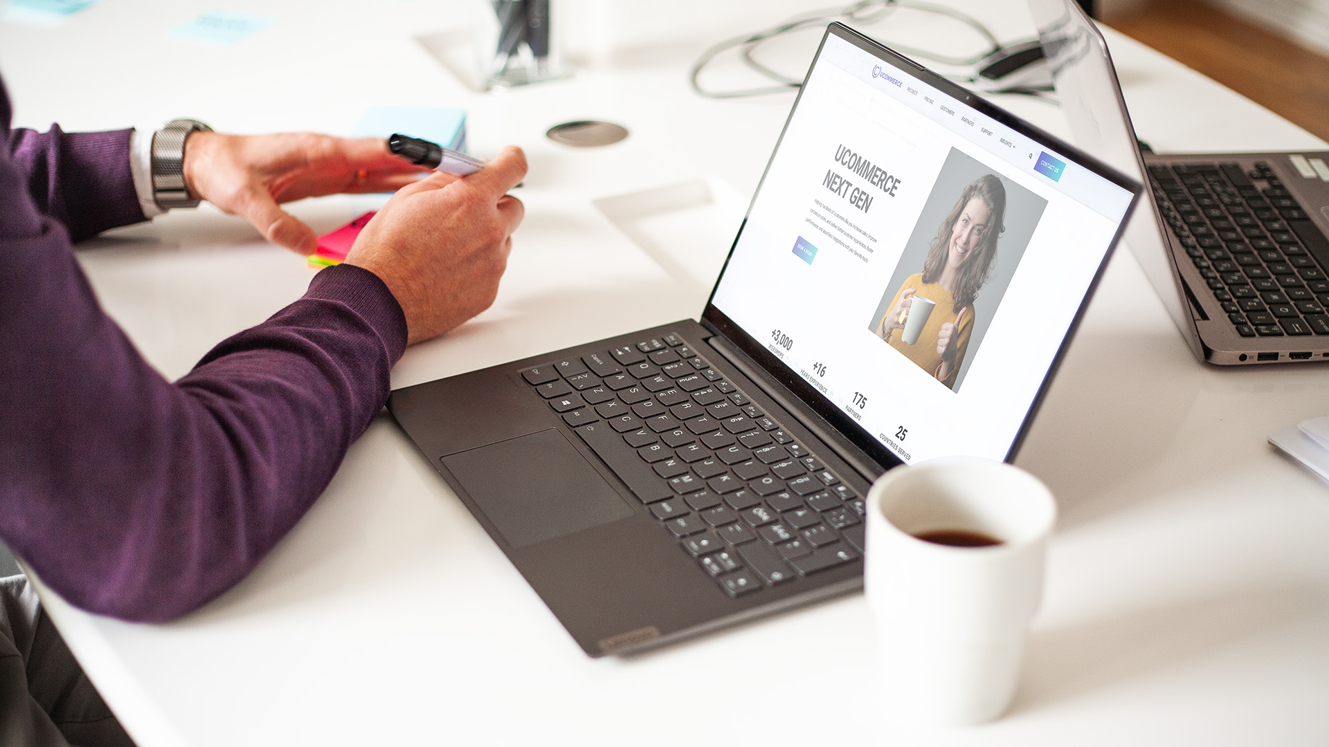 Person som sitter vid en laptop och skriver på en lapp med en kopp kaffe bredvid.