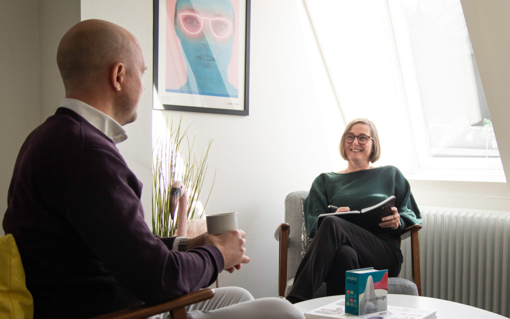 Två personer i ett informellt möte. Sitter i varsin fåtölj och diskuterar glatt.