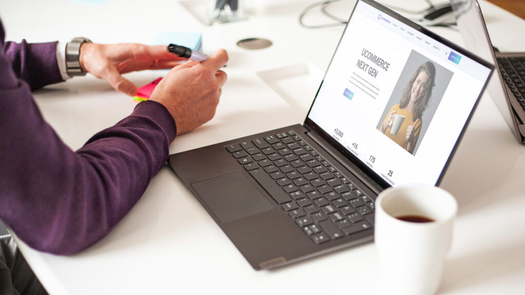 En man som skriver något på en postit-lapp. Går inte att se vad han skriver. På bordet står en laptop.