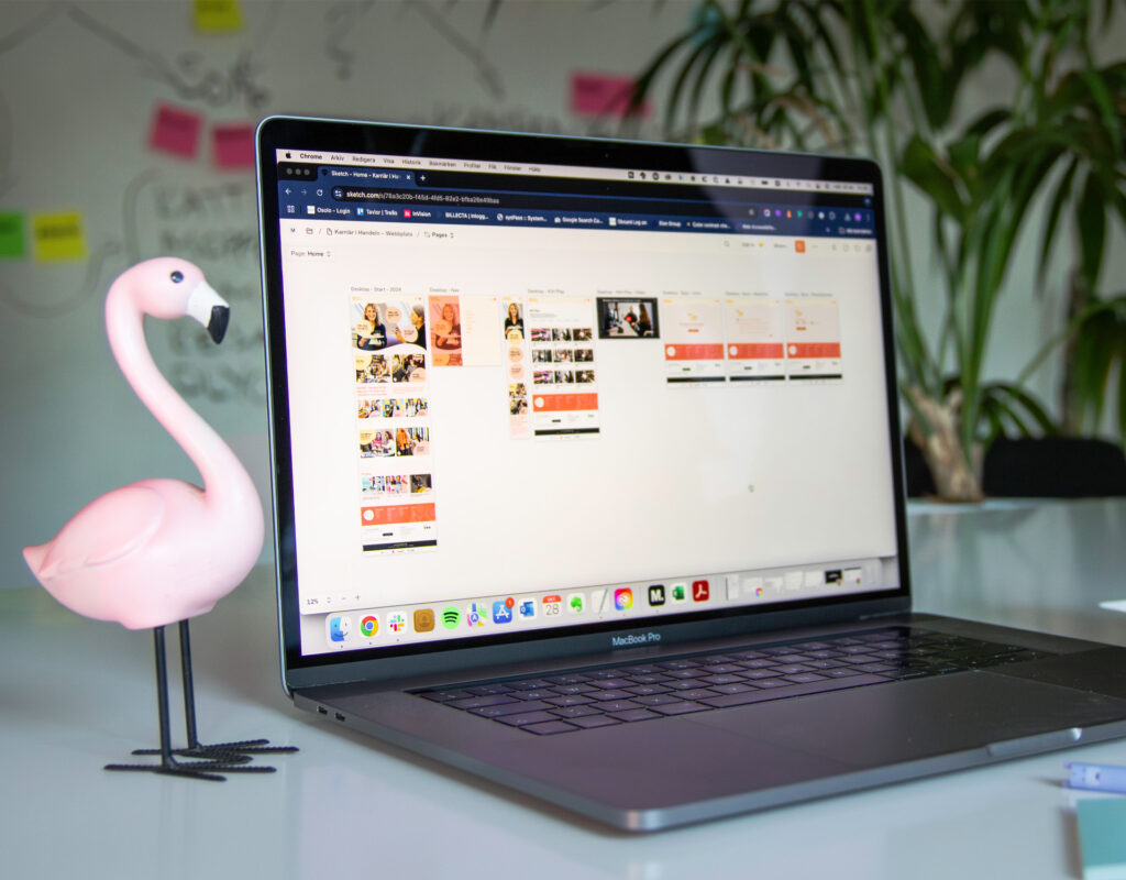 En liten plastflamingo står på bordet bredvid en öppnad laptop.