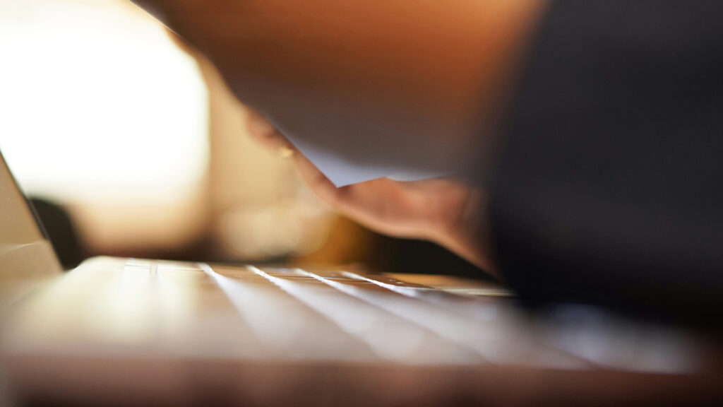 Närbild på ett tangentbord och händer som håller i papper. Nästan som en abstrakt bild eftersom stora delar är i oskärpa.