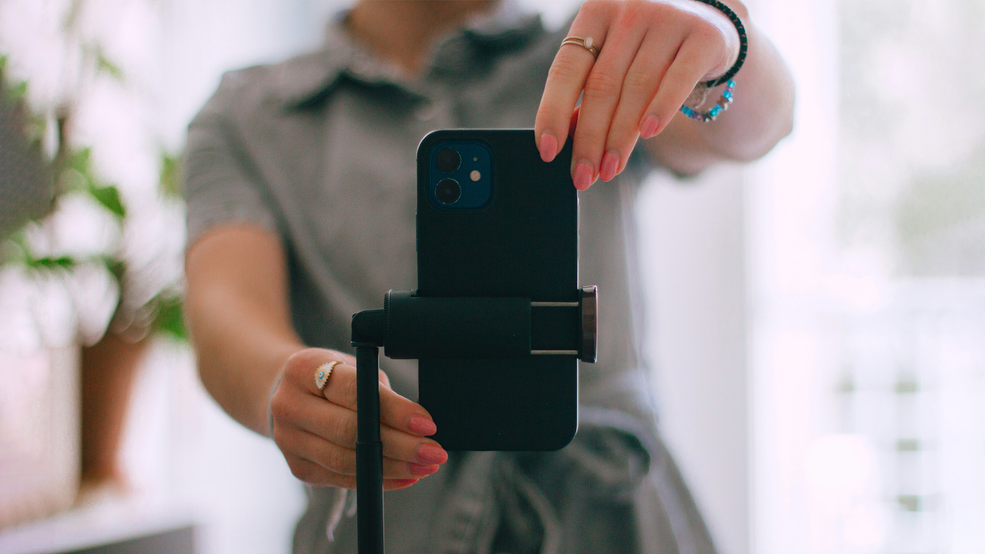 I förgrunden en mobiltelefon på ett stativ som en person håller på att förbereda för filminspelning.