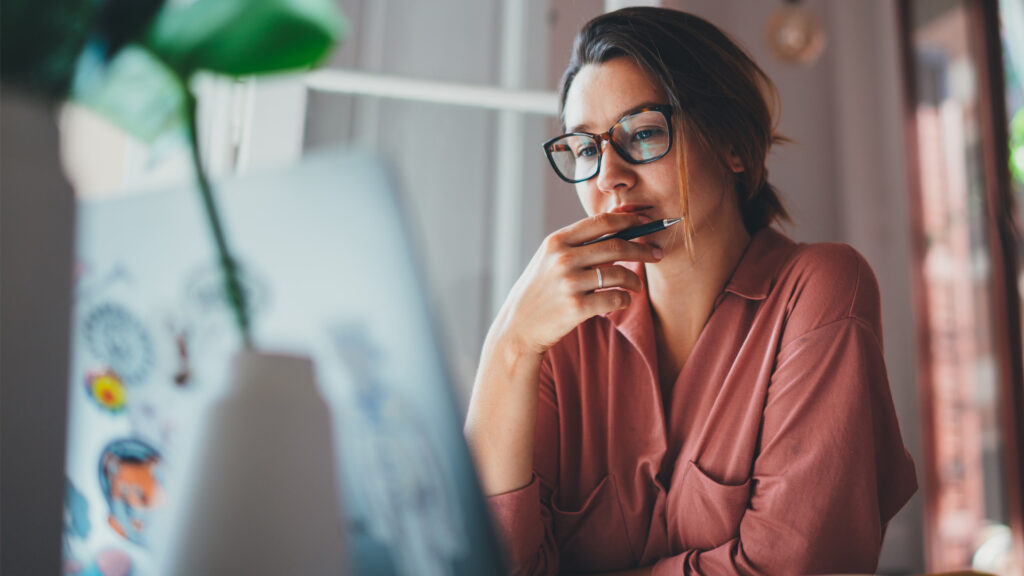 Kvinna funderar vid sin laptop.