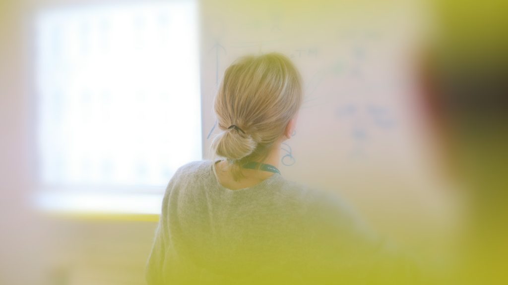En kvinna står vid en whiteboard under en workshop.