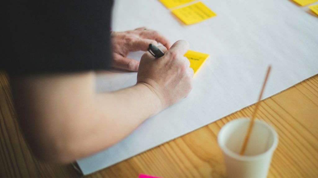 Person som jobbar i en workshop genom att skriva på en postit-lapp.