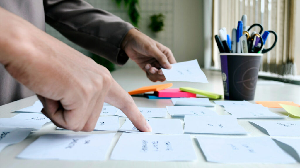 I närbild två personers händer som jobbar med postitlappar för att sätta ett användarflöde i digital lösning