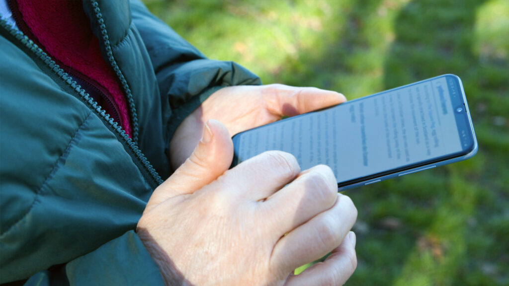 Närbild på en äldre persons händer som använder mobiltelefon
